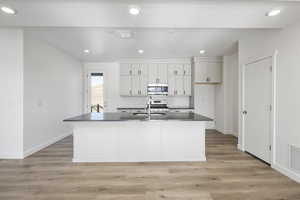 Kitchen featuring white cabinets, appliances with stainless steel finishes, a kitchen island with sink, and sink