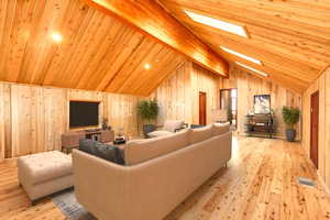 Living room featuring beamed ceiling, a skylight, wooden walls, and wood ceiling