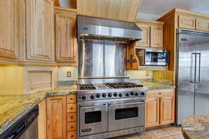 Kitchen featuring high end appliances, light stone countertops, a textured ceiling, light tile patterned flooring, and extractor fan