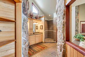 Bathroom featuring vanity, vaulted ceiling, and tiled shower