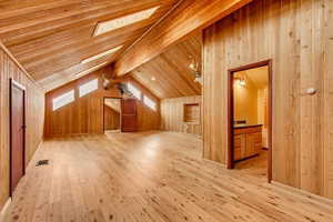 Additional living space featuring wooden walls, light hardwood / wood-style flooring, wood ceiling, and lofted ceiling with skylight