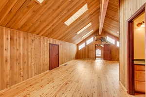 Additional living space featuring vaulted ceiling with skylight, light wood-type flooring, wooden ceiling, and wooden walls