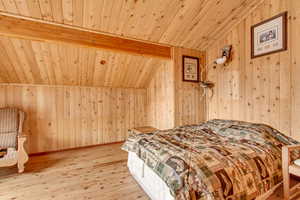 Bedroom featuring light wood-type flooring, vaulted ceiling with beams, wood walls, and wood ceiling