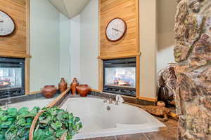 Bathroom with a multi sided fireplace, tiled bath, and wooden walls