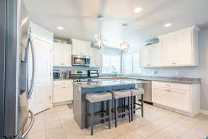 Kitchen with white cabinetry, light stone countertops, stainless steel appliances, decorative light fixtures, and a kitchen island