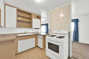 Kitchen with white gas stove, white cabinetry, and sink