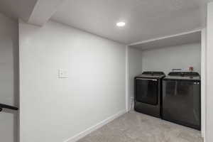 Washroom featuring light colored carpet, independent washer and dryer, and a textured ceiling