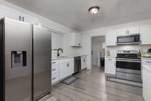 Kitchen with sink, white cabinets, stainless steel appliances, and light wood-type flooring