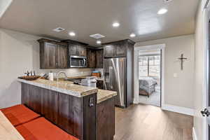 Kitchen featuring kitchen peninsula, light hardwood / wood-style flooring, appliances with stainless steel finishes, dark brown cabinetry, and a breakfast bar area