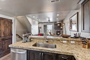 Kitchen featuring light stone countertops, dark brown cabinetry, stainless steel dishwasher, and sink