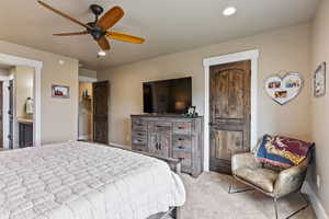 Bedroom featuring ceiling fan, ensuite bathroom, and light colored carpet