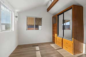 Unfurnished bedroom with vaulted ceiling with beams and light vinyl plank flooring