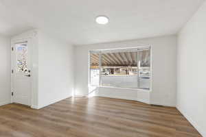 Unfurnished family room with vinyl plank flooring, a textured ceiling, and vaulted ceiling