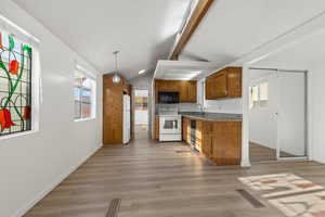 Kitchen featuring sink, lofted ceiling with beam, light vinyl plank floors, decorative light fixtures, and appliances