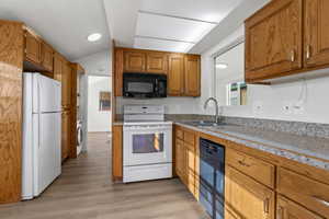 Kitchen featuring sink, light vinyl plank flooring, lofted ceiling, washer / dryer, and appliances