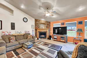 Living room featuring carpet flooring, ceiling fan, a stone fireplace, and vaulted ceiling