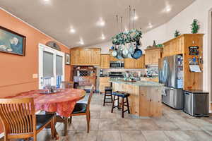 Kitchen with light stone countertops, a center island, stainless steel appliances, lofted ceiling, and a breakfast bar area