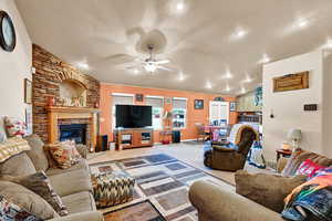 Carpeted living room featuring a textured ceiling, ceiling fan, a fireplace, and vaulted ceiling