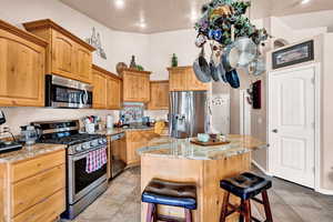 Kitchen featuring a breakfast bar area, light stone counters, a kitchen island, and appliances with stainless steel finishes