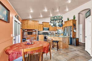 Kitchen with a center island, lofted ceiling, light stone counters, appliances with stainless steel finishes, and a kitchen bar