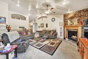 Living room with a fireplace, light colored carpet, ceiling fan, and lofted ceiling