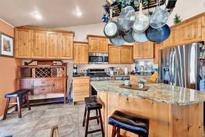 Kitchen with a breakfast bar, sink, vaulted ceiling, light stone countertops, and appliances with stainless steel finishes