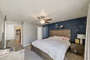 Carpeted bedroom with ceiling fan, a walk in closet, a textured ceiling, and a closet