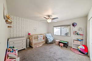 Carpeted bedroom with a textured ceiling, ceiling fan, and a crib