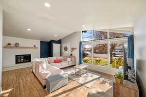 Living room with a large fireplace, light wood-type flooring, and vaulted ceiling