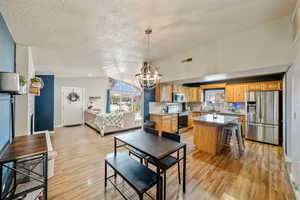 Dining room with sink, vaulted ceiling, a textured ceiling, light hardwood / wood-style floors, and a chandelier