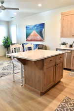 Kitchen with stainless steel dishwasher, ceiling fan, light wood-type flooring, a kitchen island, and a kitchen bar