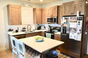 Kitchen with sink, stainless steel appliances, backsplash, a breakfast bar, and light wood-type flooring