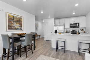 Kitchen with laminate flooring, white cabinetry, a kitchen bar, kitchen peninsula, and stainless steel appliances