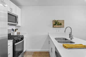 Kitchen featuring white cabinetry, sink, stainless steel appliances, and laminate flooring