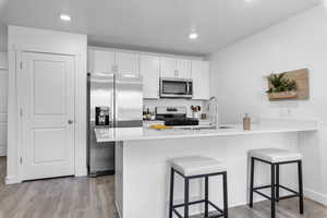 Kitchen with a kitchen breakfast bar, kitchen peninsula, white cabinetry, and appliances with stainless steel finishes