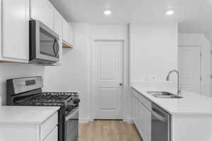 Kitchen featuring sink, white cabinets, stainless steel appliances, and laminate flooring