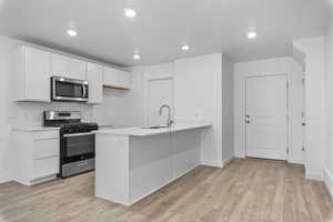 Kitchen featuring white cabinets, sink, appliances with stainless steel finishes, laminate flooring, and kitchen peninsula