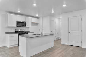 Kitchen featuring sink, white cabinetry, stainless steel appliances, and an island with sink