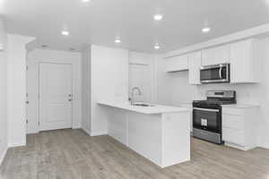 Kitchen featuring kitchen peninsula, laminate flooring, stainless steel appliances, sink, and white cabinets