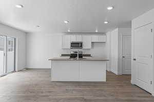 Kitchen with white cabinetry, a center island with sink, stainless steel appliances, and light wood-type flooring