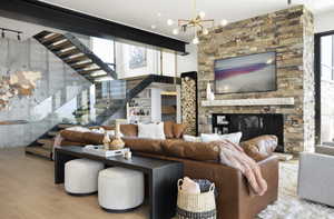 Living room featuring light wood-type flooring, a stone fireplace, and a notable chandelier