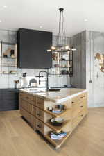 Kitchen with light hardwood / wood-style floors, light stone counters, hanging light fixtures, and sink