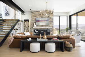 Living room with an inviting chandelier, a stone fireplace, and light hardwood / wood-style flooring