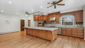 Kitchen with light wood-type flooring, stainless steel appliances, tile countertops, a center island with sink, and a baseboard radiator