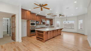 Kitchen featuring black microwave, maple hardwood flooring, ventilation hood, decorative light fixtures, and a center island with sink