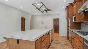 Kitchen featuring tile countertops, a center island with sink, sink, ceiling fan, and extractor fan