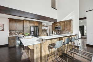 Kitchen featuring wine cooler, dark hardwood / wood-style floors, appliances with stainless steel finishes, beamed ceiling, and a breakfast bar area