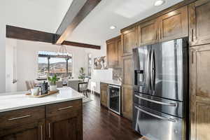 Kitchen featuring dark hardwood / wood-style floors, decorative light fixtures, beam ceiling, stainless steel fridge with ice dispenser, and beverage cooler