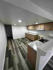 Kitchen featuring dark wood-type flooring, brown cabinetry, a sink, a peninsula, and baseboards