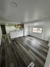 Unfurnished living room featuring visible vents, vaulted ceiling, baseboards, and dark wood finished floors